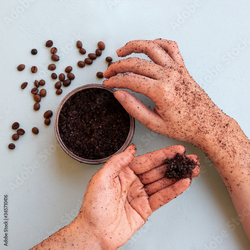 Top view of female hands and a jar with roasted coffee bean scrub and sea salt on mint background in square format. Rejuvenating scrub in round jar for skin exfoliation.
