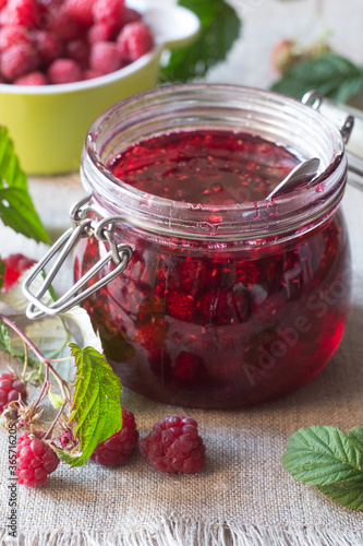 Raspberry jam in glass jar and berries on table