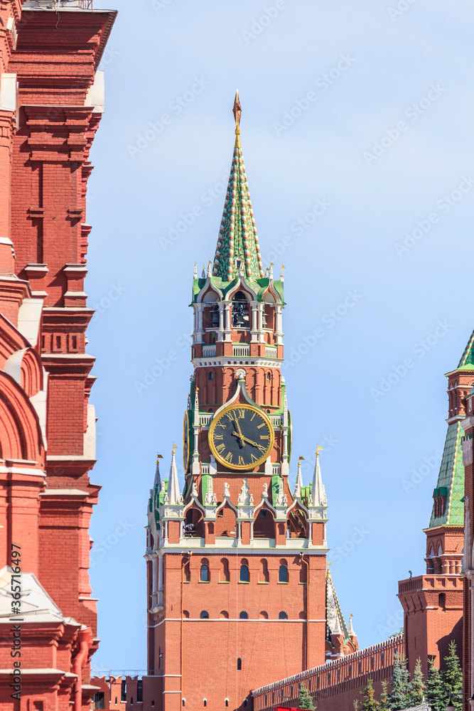 View of Spasskaya Tower with large clock of Moscow Kremlin built from red bricks on a summer morning. Clear blue sky in the background. Theme of travel in Russia.