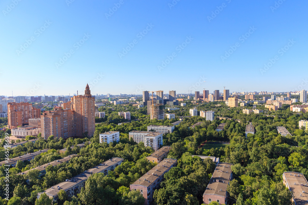 High angle view of Moscow city shortly before sunset. Residential buildings stands between green trees. Clear blue sky.