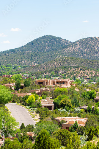 Vertical landscape view in Santa Fe, New Mexico mountains of road street through community neighborhood with green plants summer and adobe traditional houses photo