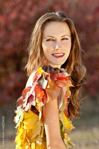 Beautiful autumn woman in bright dress from fallen leaves in golden autumn scenery