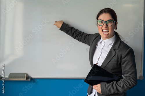 Angry business woman coach points finger to white board in office.A disgruntled female boss is holding a tablet and screaming at subordinates in the presentation room. Planer in the conference room.