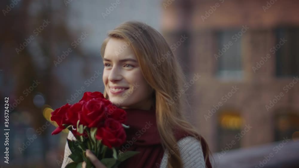 Sweet girl smelling bouquet flowers outside. Cute woman carrying roses on street Sweet girl smelling bouquet flowers outside. Cute woman carrying roses on street