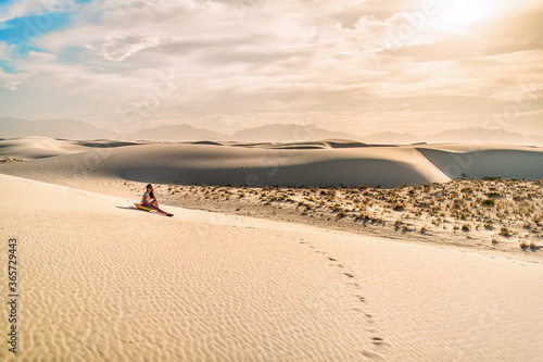 Young woman girl on sand in white sands dunes national monument in New Mexico sitting on disk sled for sliding down hill during vintage tone sunset