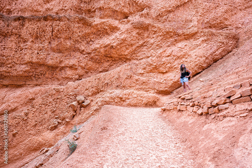 Woman person standing by red color formations at Queens Garden Navajo Loop trail at Bryce Canyon National Park in Utah with camera looking up from steep switchback