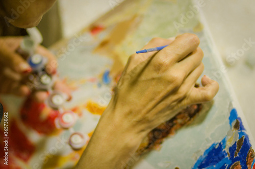 Brush in the hand of an artist drawing a picture on the canvas