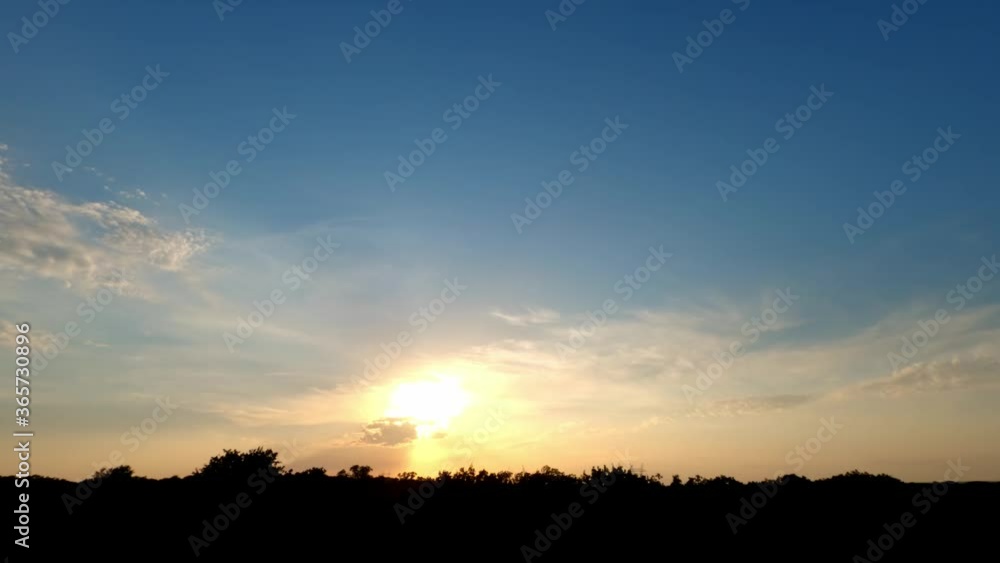 Time lapse of sunset over treetops in rural landscape with no buildings; with some light scattered clouds passing towards the viewer Time lapse of sunset over treetops in rural landscape with no buildings; with some light scattered clouds passing towards the viewer