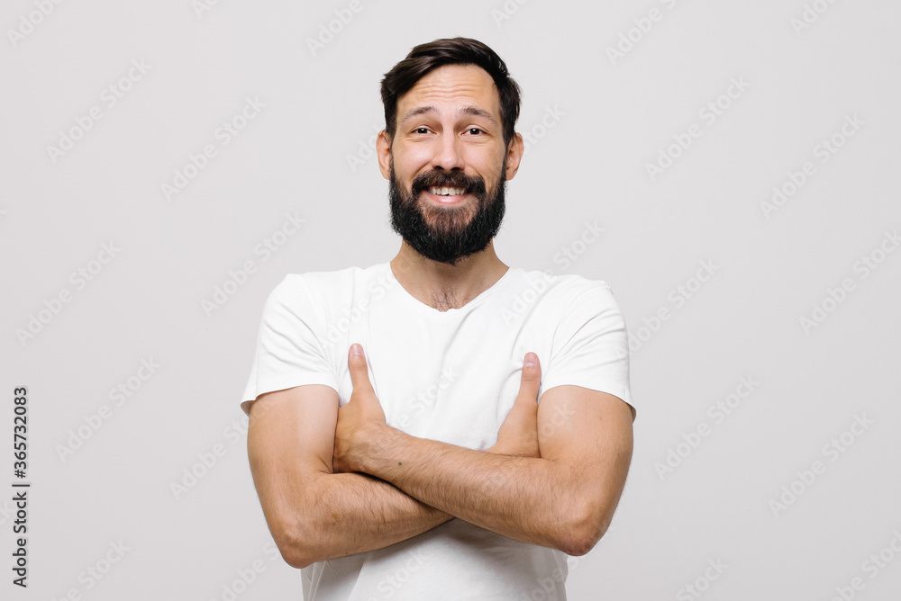 Studio portrait of surprised pretty young man with short haircut standing over white background, looking puzzled to camera with crossed arms on his chest Studio portrait of surprised pretty young man with short haircut standing over white background, looking puzzled to camera with crossed arms on his chest