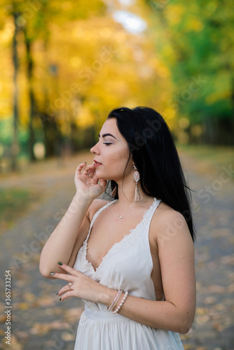 Young beautiful brunette female in a long white dress in autumn park.