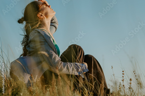 Portrait of a woman with sun glasses looking up in field at sunset 