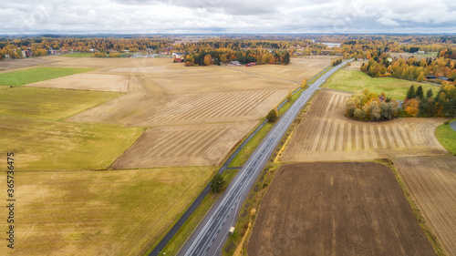 Aerial view of country road, autumn trees and ploughed fields. Aerial panorama of beautiful farmlands 