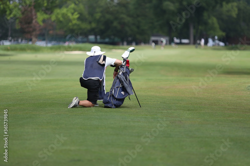 A golf caddie kneels down in the fairway
