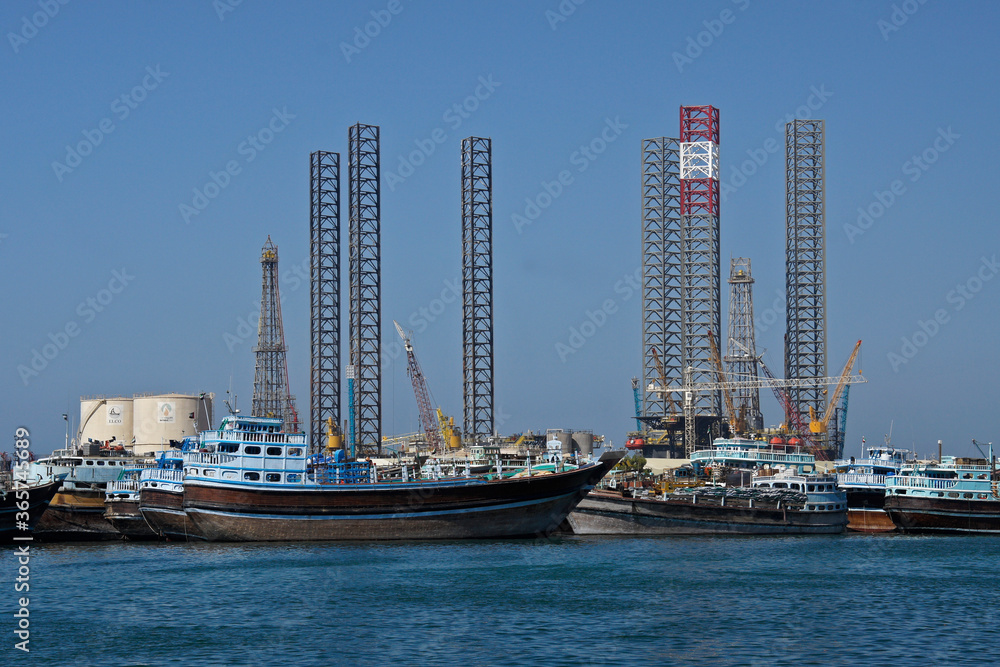 Obraz premium Boats, cranes, oil derricks, towers, and oil tanks are clustered at one end of Sharjah Creek, Sharjah, United Arab Emirates