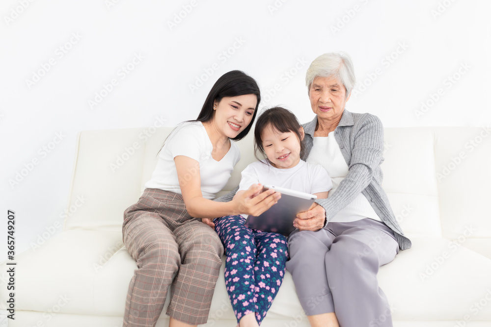 old Asian female and her family connect internet with tablet computer, they feeling happy and smile, they sitting on sofa, mother's day and happiness family time, technology and social network