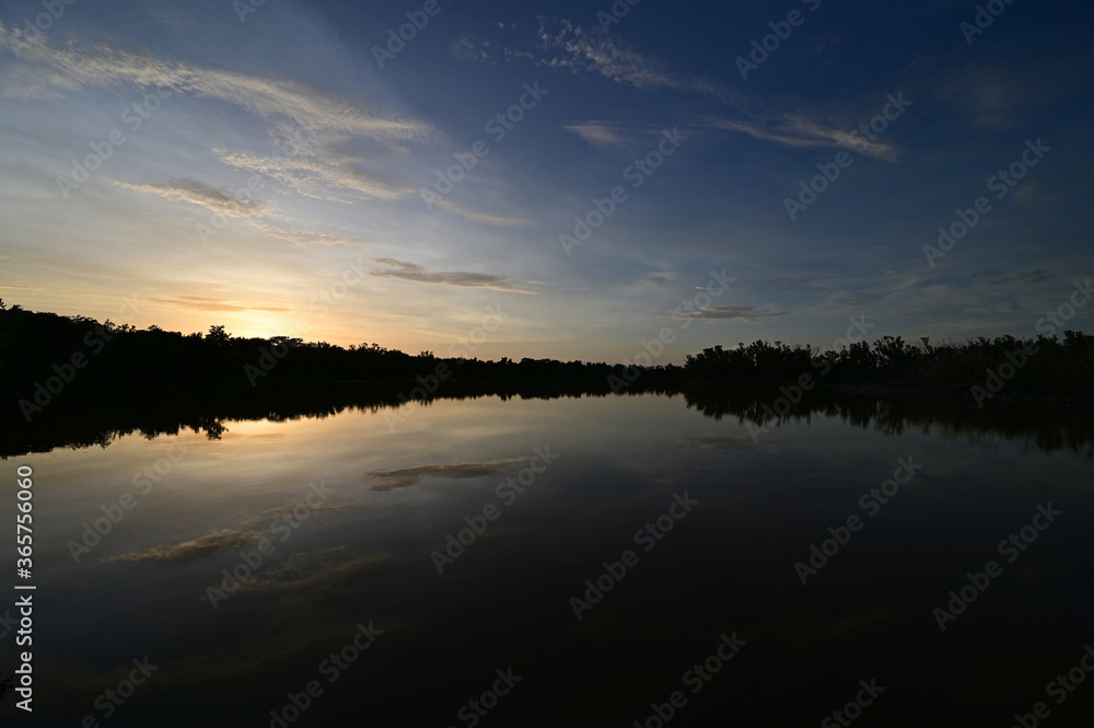 Brilliant colorful clouds in twilight reflected on calm water of Eco Pond in Everglades National Park, Florida on summer evening.