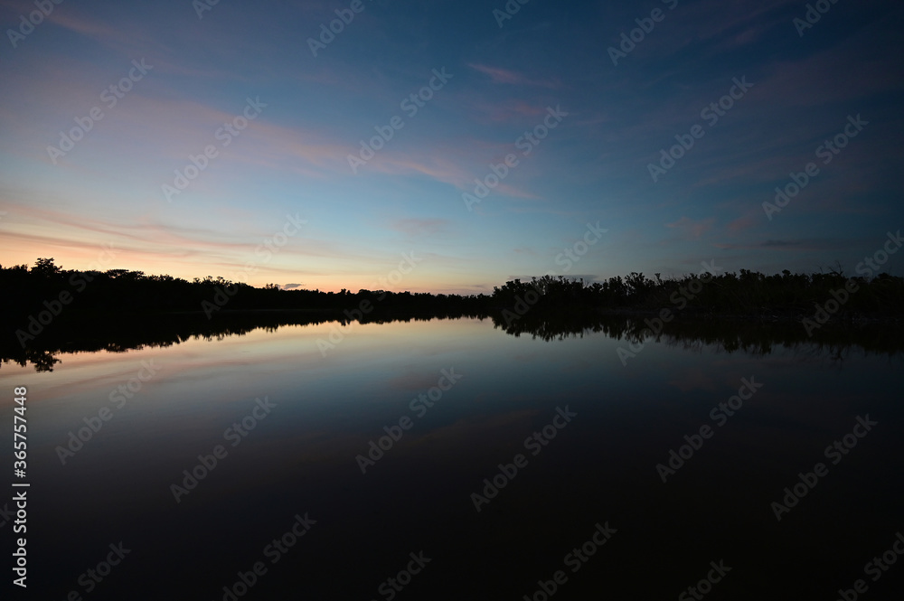 Brilliant colorful clouds in twilight reflected on calm water of Eco Pond in Everglades National Park, Florida on summer evening.