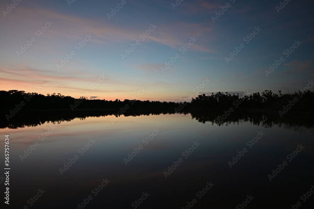 Brilliant colorful clouds in twilight reflected on calm water of Eco Pond in Everglades National Park, Florida on summer evening.