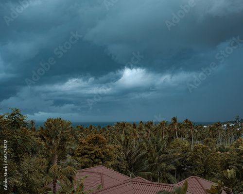 Dramatic stormy clouds before the rain over trees and sea on tropical island. 