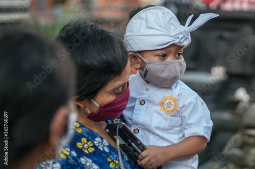 Balinese mother and child are wearing traditional clothes during the corona pandemic or covid-19. They both use masks to protect themselves from virus attacks. They prepare to pray at the temple