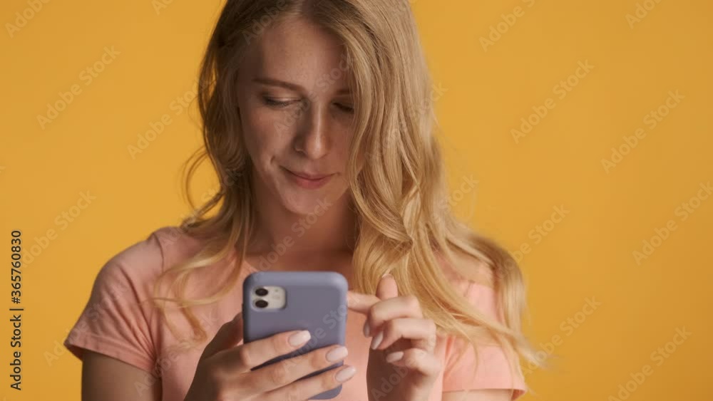 Young concentrated blond woman intently using smartphone on camera over colorful background Young concentrated blond woman intently using smartphone on camera over colorful background
