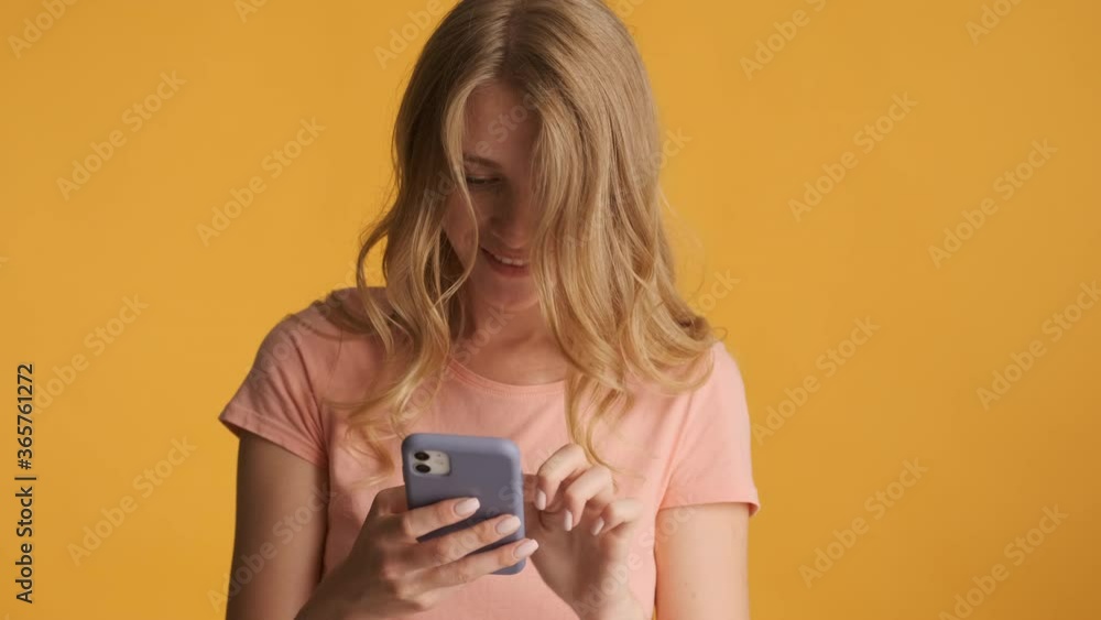 Young excited blond girl intently using smartphone on camera over colorful background. Wow expression Young excited blond girl intently using smartphone on camera over colorful background. Wow expression