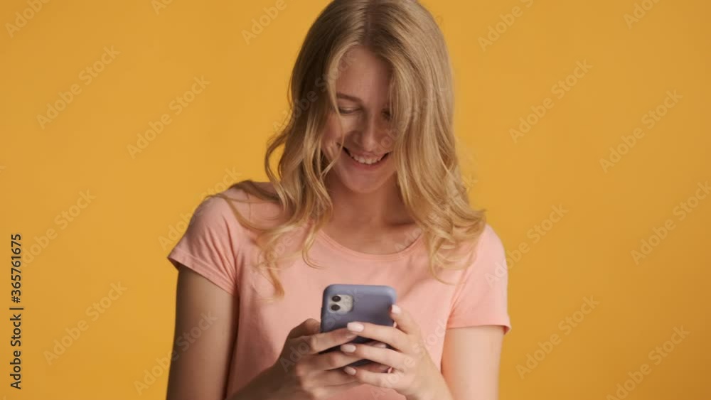Attractive smiling blond girl joyfully using smartphone on camera over colorful background. Wow expression Attractive smiling blond girl joyfully using smartphone on camera over colorful background. Wow expression