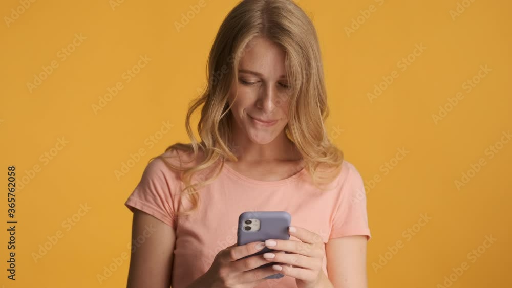 Attractive blond girl happily using smartphone on camera over colorful background Attractive blond girl happily using smartphone on camera over colorful background