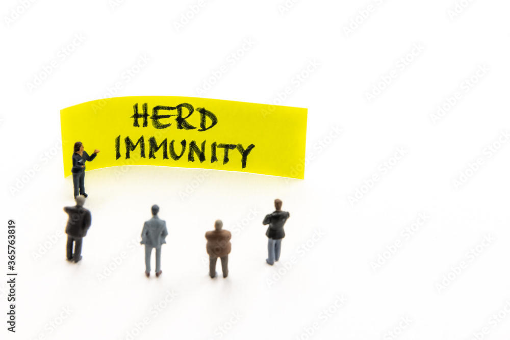 Meeting with miniature figurines posed as business people standing around post-it note with Herd Immunity handwritten message in background, minimalist abstract concept with focus on text Meeting with miniature figurines posed as business people standing around post-it note with Herd Immunity handwritten message in background, minimalist abstract concept with focus on text