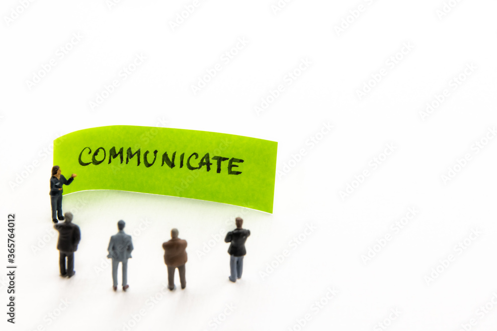 Meeting with miniature figurines posed as business people standing around post-it note with Communicate handwritten message in background, minimalist abstract concept with focus on text Meeting with miniature figurines posed as business people standing around post-it note with Communicate handwritten message in background, minimalist abstract concept with focus on text