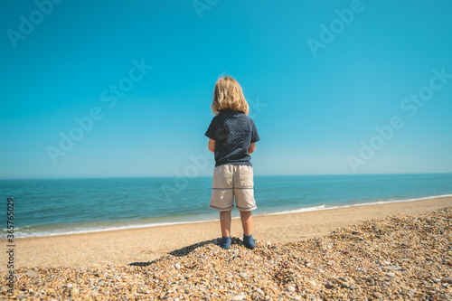 Preschooler boy standing by the sea on a sunny summer day