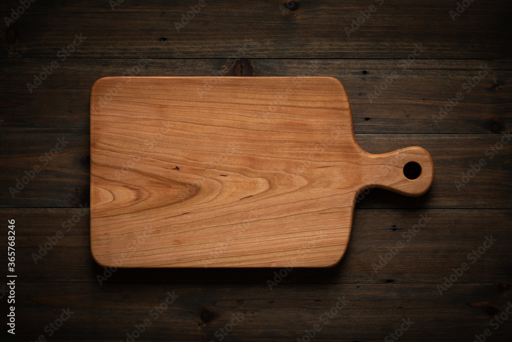 Hand-made cherry wood cutting board on the darkened wooden tabletop - obrazy, fototapety, plakaty 