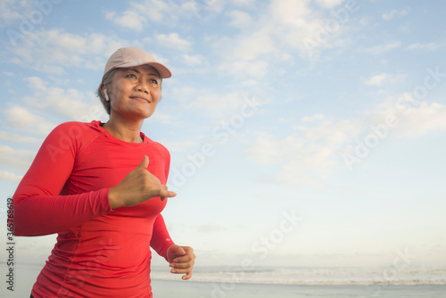 fit and happy middle aged woman running on the beach - 40s or 50s attractive mature lady with grey hair doing jogging workout enjoying fitness and healthy lifestyle