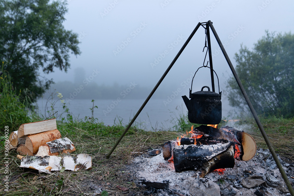 the kettle is heated on the fire in the evening. Tourist camping by the river. travel to Siberia. picturesque evening view the kettle is heated on the fire in the evening. Tourist camping by the river. travel to Siberia. picturesque evening view