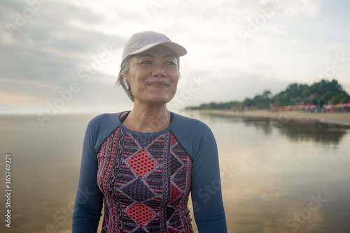portrait of fit and happy middle aged woman after beach running workout - 40s or 50s attractive mature lady with grey hair smiling cheerful after jogging enjoying fitness healthy lifestyle
