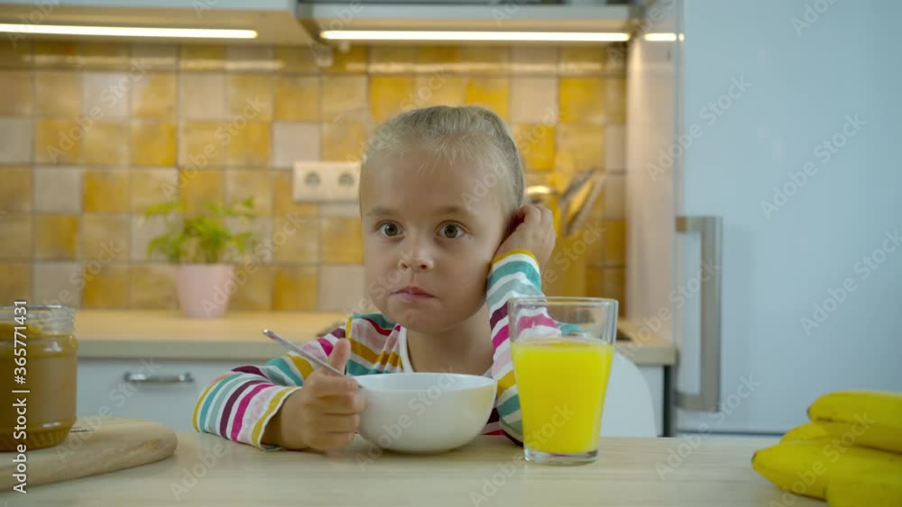 Little hungry girl eating flakes with milk and drinking juice Little hungry girl eating flakes with milk and drinking juice