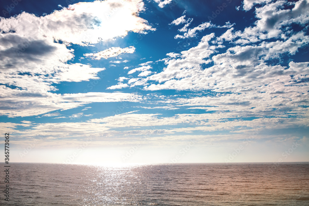 The seascape of the noon in the Mediterranean sea: sun, clouds, horizon and ripples of waves on the sea surface.