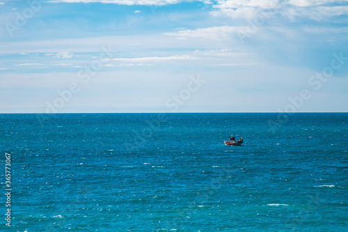 Small ship sailing on the horizon in a waving sea and cloudy sky.