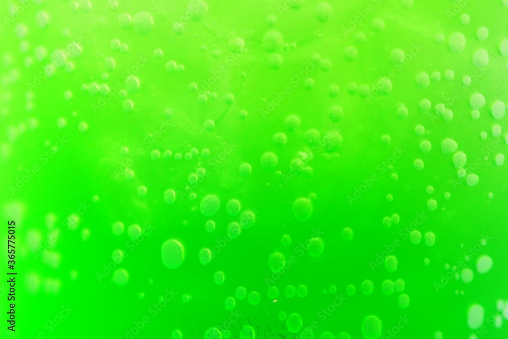 Closeup of bubbles and ice of bright green juice in a clear glass for background and decoration for drinks