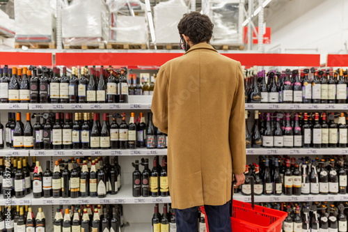 Фотография A young man in a supermarket chooses alcohol in the wine section