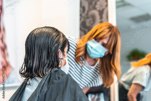 Hairdresser with face mask cutting hair to client. Safety measures for hairdressers in the Covid-19 pandemic. New normal, coronavirus, social distance