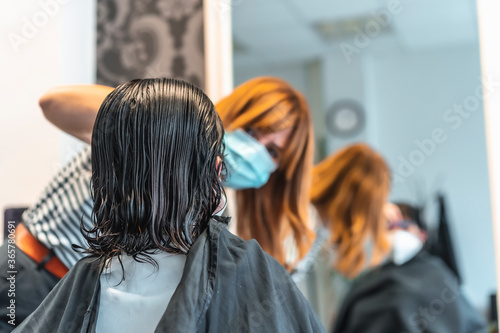 Young brunette girl with mask in a hairdresser cutting her hair. Reopening with security measures for hairdressers in the Covid-19 pandemic. New normal, coronavirus, social distance