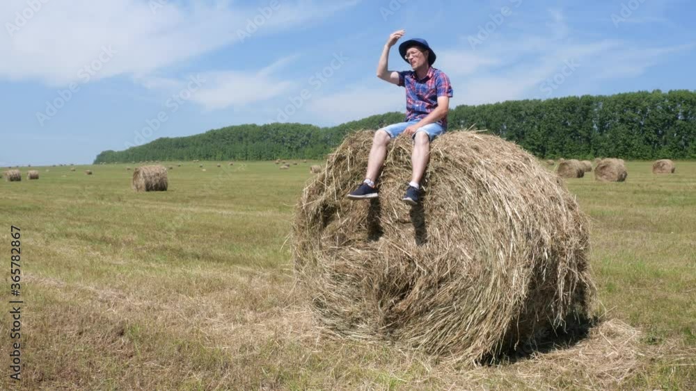 A man sits on a haystack and then lies down. A man sits on a haystack and then lies down.