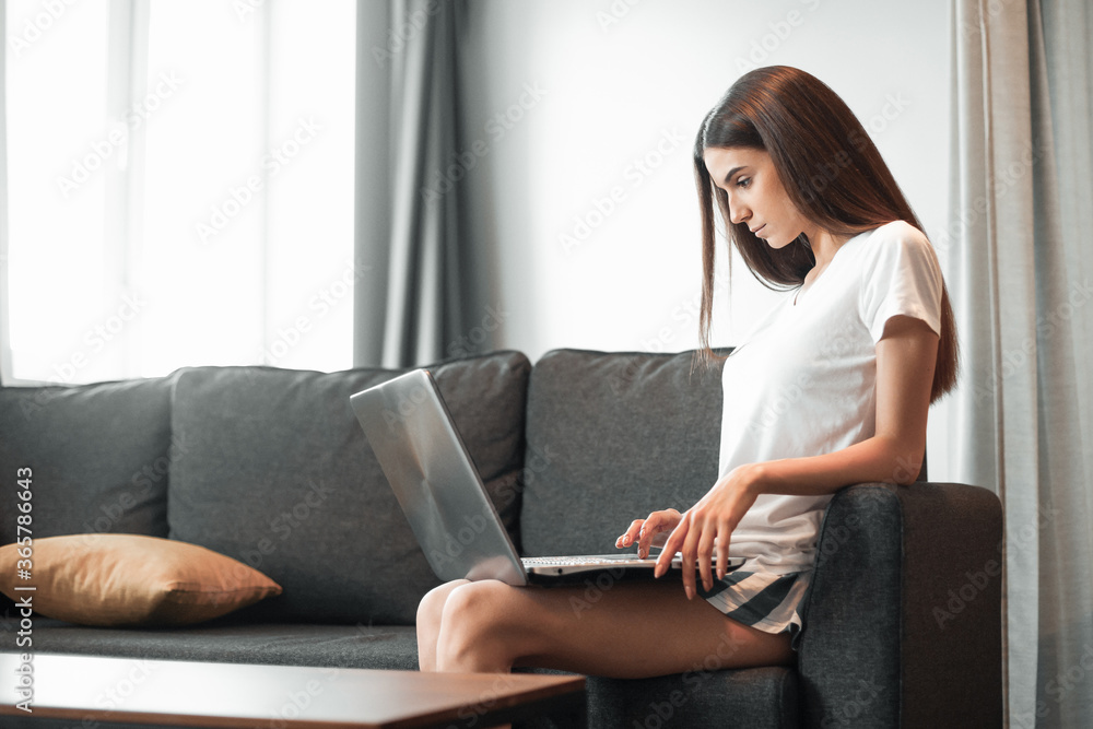 Young woman with modern laptop sitting on sofa at home