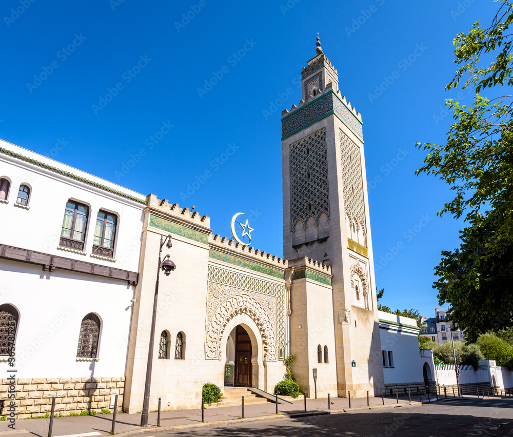 General view of the entrance of the Great Mosque of Paris, France, at the foot of the 33-meter high minaret, with the star and crescent above the doorway against blue sky.