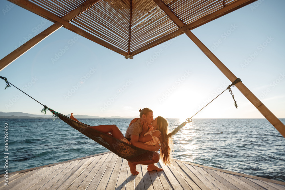 Stockfoto Relaxing time during vacation. Happy honeymoon couple in Maldives  on hammock with beach and sea in the background, hug and kiss each other,  sunset time | Adobe Stock