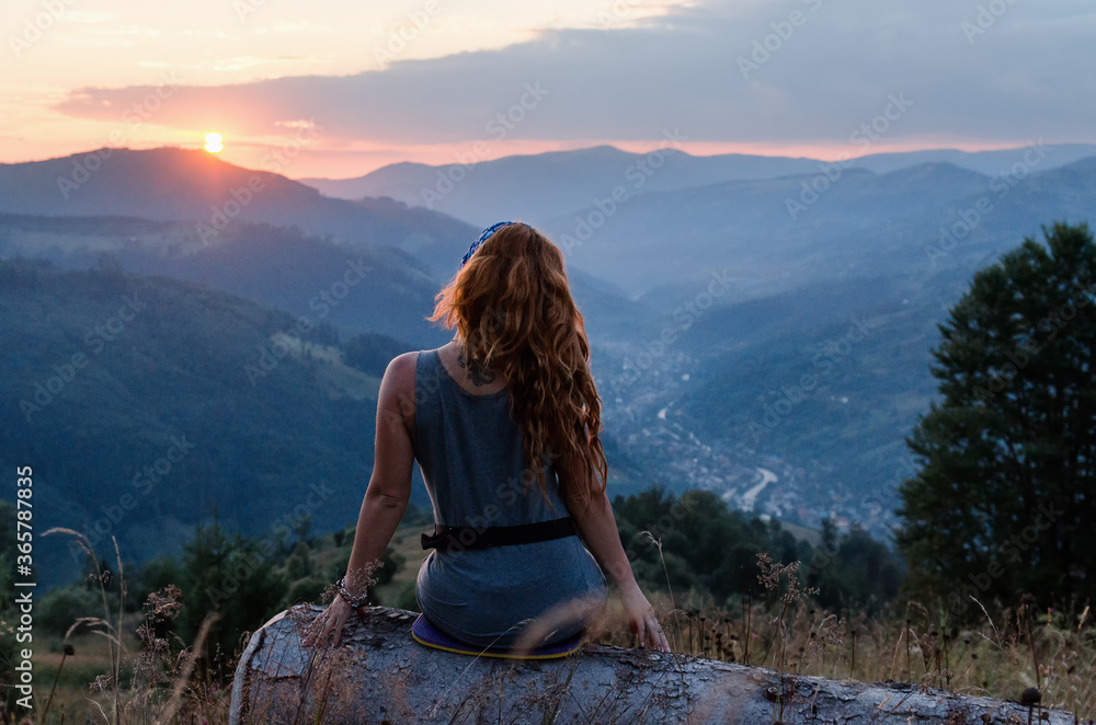 A girl sits on the edge of the cliff and looking at the sun valley and mountains. Woman sitting on mountain top and contemplating the sunset. Sunset in Ukrainian Carpathians