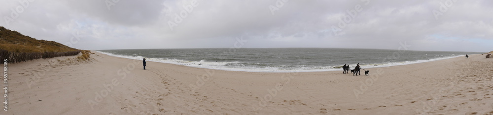 Panorama shot of the west beach from the island of Sylt Germany, dunes, sandy beach, surf on a cold wet day in winter, the beach walkers are dressed accordingly. The picture reflects the vastness Panorama shot of the west beach from the island of Sylt Germany, dunes, sandy beach, surf on a cold wet day in winter, the beach walkers are dressed accordingly. The picture reflects the vastness