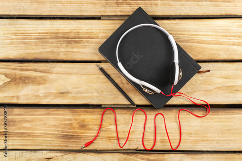 Black notepad, headphones, coffee on a wooden background.