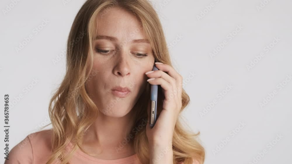 Attractive blond girl chewing gum confidently talking on smartphone over gray background Attractive blond girl chewing gum confidently talking on smartphone over gray background